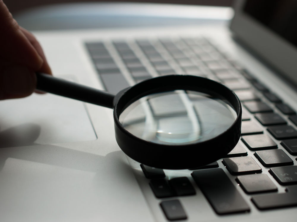 A photo of a magnifying glass being held over the keyboard of a laptop